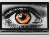 Close-up of human eye with orange iris on laptop screen representing digital surveillance